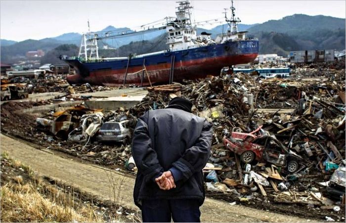 Starejši Japonec gleda s hriba na mesto Ishinomaki, ki ga je opustošil cunami. 2011 g